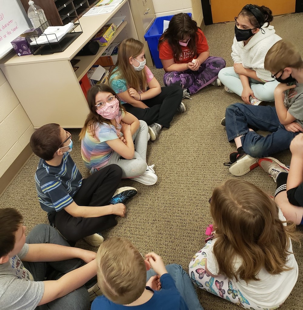 Group of masked 4th grade students sitting on floor petting a white rat