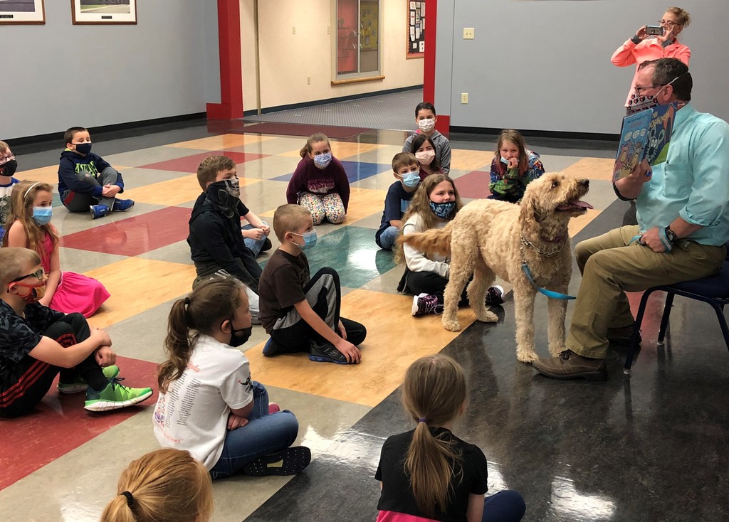 Kids listening to a story read by the principal and his dog