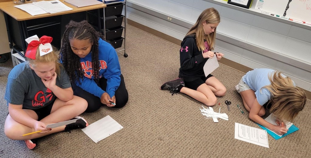 4 6th grade girls work on assignments on the floor of their classroom