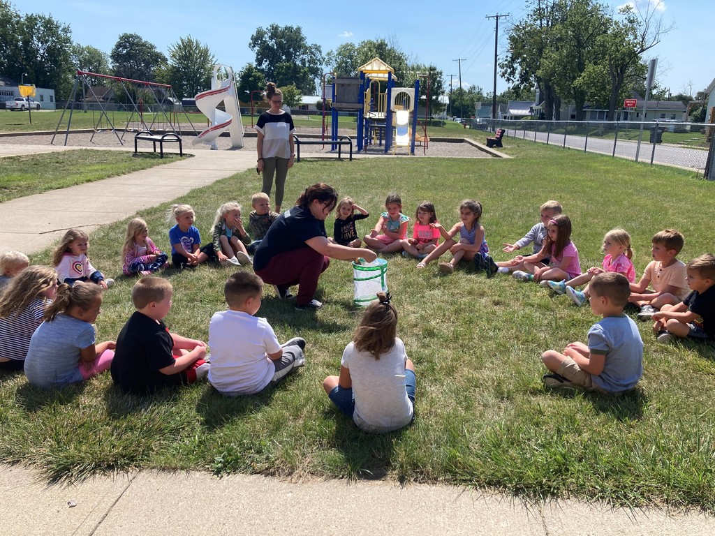 Kindergarten students sit outside learning about butterflies