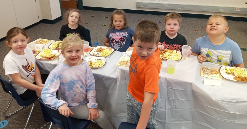 Kindergarten students smile as they eat a Thanksgiving meal